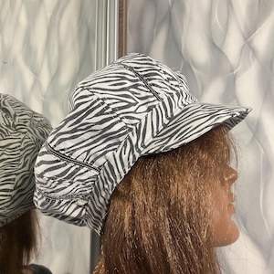 Peut inclure: Casquette à rayures zébrées avec une visière incurvée. Le chapeau présente un motif noir et blanc, avec des détails de couture noirs. La casquette est en tissu doux et est conçue pour être portée sur la tête.