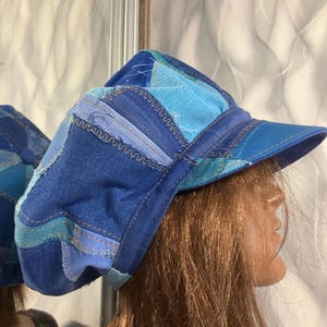 May include: A patchwork denim hat in shades of blue, light blue, and teal. The hat features a curved brim and is constructed from various denim pieces sewn together with visible stitching. The hat is a unique accessory.
