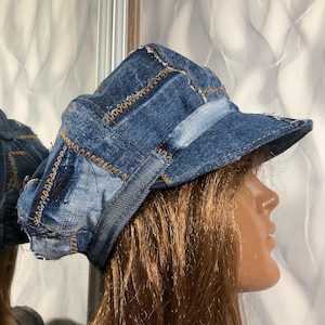 May include: A denim patchwork hat with a short brim. The hat is constructed from various shades of blue denim, stitched together with contrasting gold thread. The hat's design features a newsboy style with a slightly rounded crown.