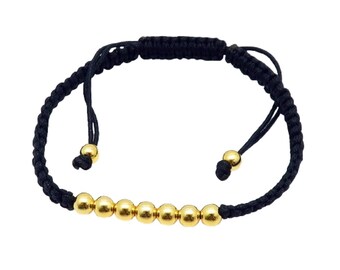 May include: A black braided bracelet with gold beads. The bracelet has adjustable ties on each end.