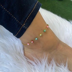 May include: Gold anklet with a chain and colorful evil eye charms. The charms are round and have a white center with a blue, green, pink, or yellow outer ring.