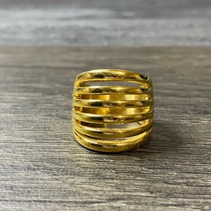 May include: A gold-toned ring with a wide band featuring multiple horizontal lines.