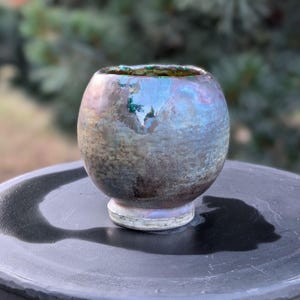 May include: A handcrafted ceramic bowl with a unique iridescent glaze. The bowl has a rounded shape with a small, sturdy base. The colors shift from blue to green and purple, creating a captivating visual effect. The bowl is approximately 4 inches in diameter.
