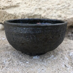 May include: A black ceramic bowl with a textured surface. The bowl is slightly wider at the top than the bottom.