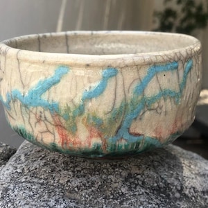 May include: A small, white ceramic bowl with a crackled glaze. The bowl has a blue, green, and orange design.