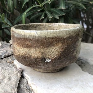 May include: A small, brown and white ceramic teacup with a crackled glaze. The cup has a wide, rounded shape and a slightly flared rim.