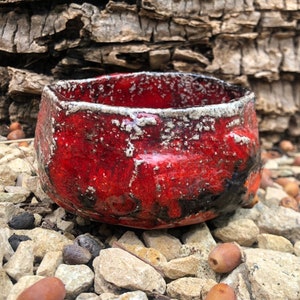 May include: A small, red ceramic bowl with a textured, speckled glaze. The bowl has a slightly irregular shape and a white rim.