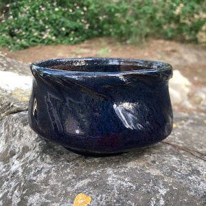 May include: A dark blue ceramic bowl with a slightly uneven rim. The bowl has a glossy finish and a subtle swirling pattern.