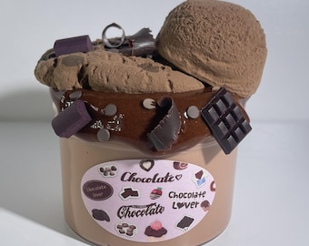 Puede incluir: Un recipiente de plástico transparente lleno de una sustancia marrón claro, cubierto con una galleta de chocolate, una bola de helado de chocolate y decoraciones de chocolate. La etiqueta del recipiente dice "Chocolate Lover".