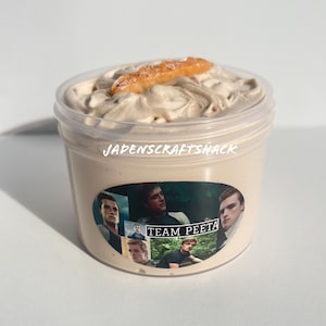 May include: A clear plastic container filled with light brown whipped cream topped with a brown cookie. The container has a sticker with the text "JADENSCRAFTSHACK" and a collage of images of a man with the text "TEAM PEETA".