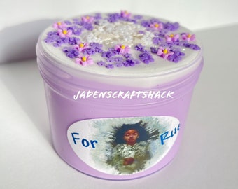 Könnte beinhalten: Lilafarbener Schleim in einem durchsichtigen Glas mit einem weißen Deckel, der mit lila und rosa Blumen verziert ist. Das Glas hat ein Etikett mit der Aufschrift "Für Rue" und "JADENSCRAFTSHACK".