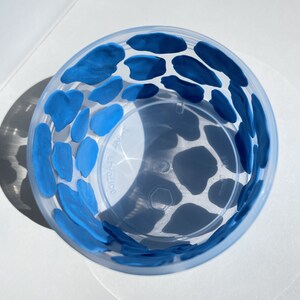 May include: A clear plastic cup with a blue cow print design. The cup is decorated with blue paint in a cow print pattern.