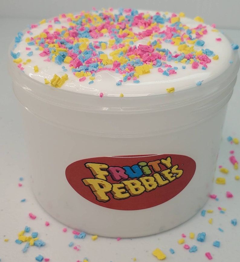 Op de afbeelding: Witte slijm met kleurrijke sprinkels in een doorzichtige plastic container met een rood label waarop "Fruity Pebbles" staat.