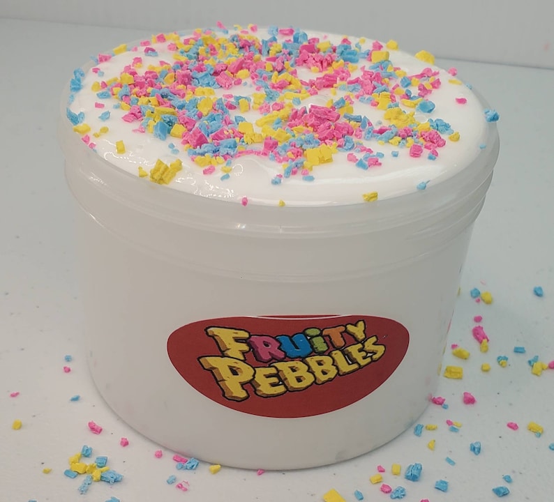 Op de afbeelding: Witte slijm met kleurrijke sprinkels in een doorzichtige plastic container met een rood label waarop "Fruity Pebbles" staat.