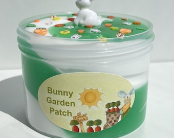 May include: A green and white slime with a bunny figurine on top. The slime is in a clear plastic container with a label that says "Bunny Garden Patch".