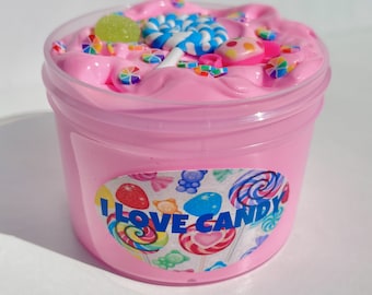 May include: Pink slime in a clear jar with a colourful candy-themed label that says "I Love Candy". The slime is topped with colourful sprinkles, a gummy candy, and a blue and white lollipop.