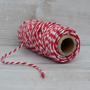 May include: A roll of red and white baker's twine with a brown cardboard center. The twine is unwinding from the roll.