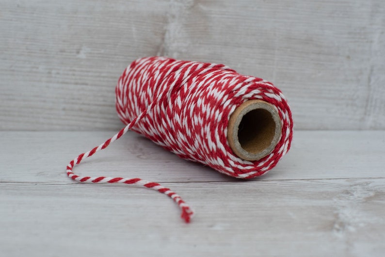 May include: A roll of red and white baker's twine with a brown cardboard center. The twine is unwinding from the roll.