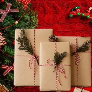 May include: Three brown paper wrapped gifts tied with red and white twine. The gifts are sitting on a red knitted surface.