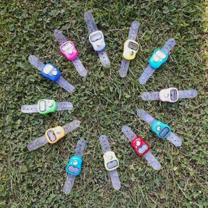 May include: A collection of twelve colorful digital tasbihs, also known as prayer beads, with clear plastic straps. Each tasbih has a digital counter display and a button to increment the count.