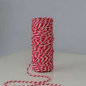 May include: A roll of red and white baker's twine with a length of twine extending from the roll.