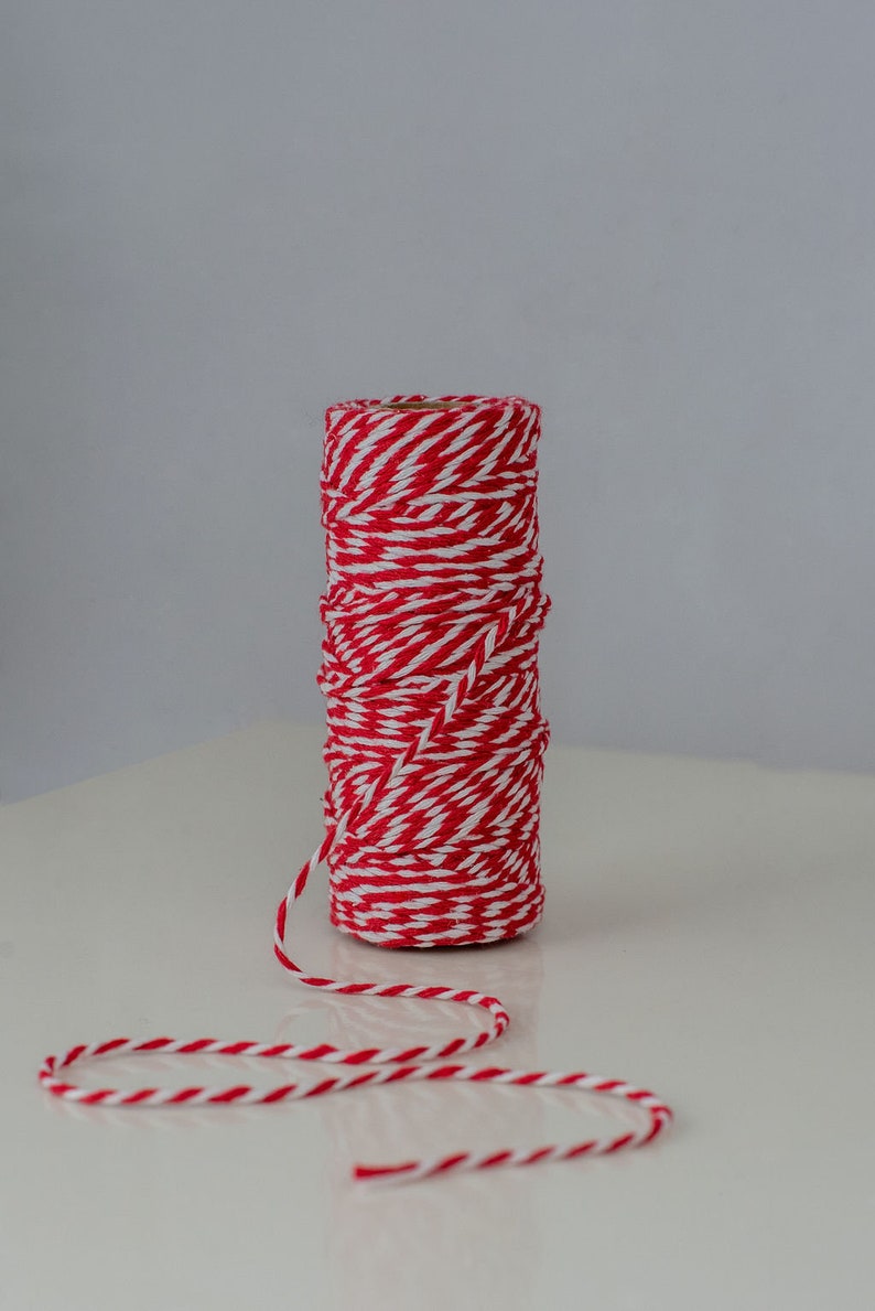May include: A roll of red and white baker's twine with a length of twine extending from the roll.