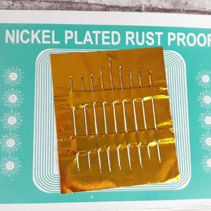 K&ouml;nnte beinhalten: Eine Packung mit 20 vernickelten, rostfreien N&auml;hnadeln in einer goldenen Folienverpackung. Die Verpackung tr&auml;gt den Aufdruck "Nickel Plated Rust Proof".