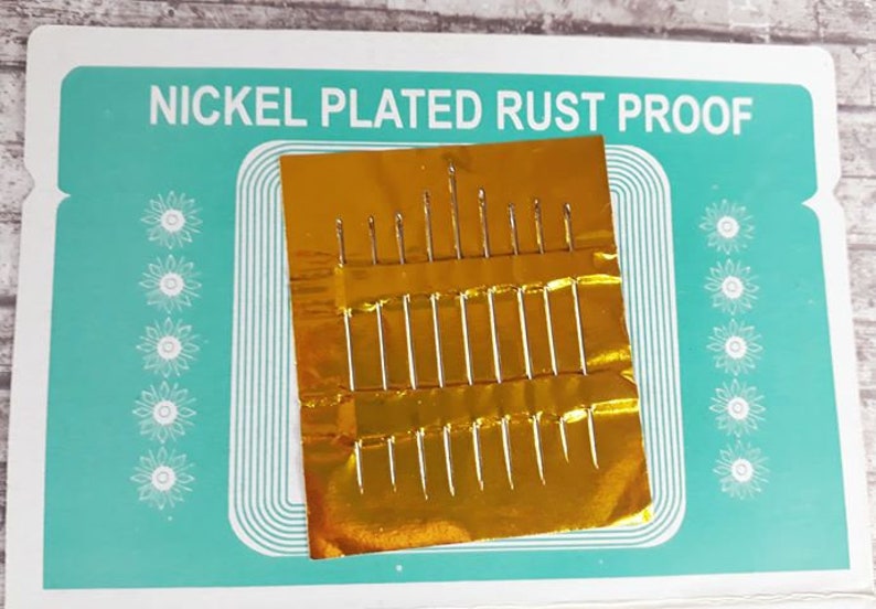 K&ouml;nnte beinhalten: Eine Packung mit 20 vernickelten, rostfreien N&auml;hnadeln in einer goldenen Folienverpackung. Die Verpackung tr&auml;gt den Aufdruck "Nickel Plated Rust Proof".