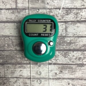 May include: A green digital tally counter with a silver button. The counter reads "31". The counter has the words "Tally Counter", "Count", and "Reset" printed on it.