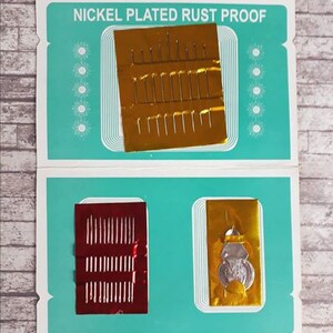 K&ouml;nnte beinhalten: Eine blaue und wei&szlig;e Karte mit dem Text "Nickel Plated Rust Proof" darauf gedruckt. Die Karte hat zwei F&auml;cher, die jeweils eine Packung Nadeln enthalten. Eine Packung ist golden und die andere rot.