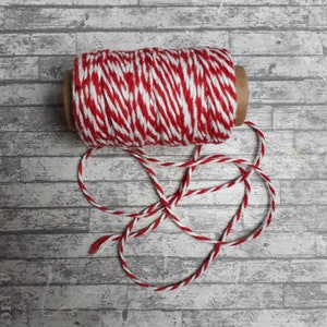 May include: A roll of red and white baker's twine with a loose end. The twine is on a white wood background.