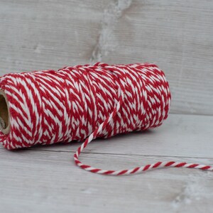 May include: A roll of red and white baker's twine. The twine is wound around a cardboard tube.