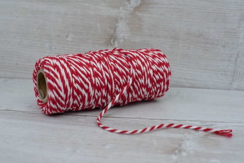 May include: A roll of red and white baker's twine. The twine is wound around a cardboard tube.