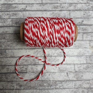 May include: A spool of red and white baker's twine with a cardboard core. The twine is wound around the core and is ready to be used for wrapping gifts or crafts.