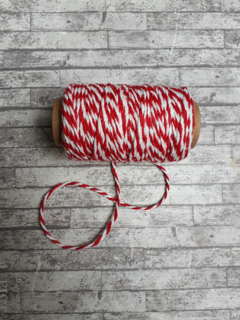 May include: A spool of red and white baker's twine with a cardboard core. The twine is wound around the core and is ready to be used for wrapping gifts or crafts.