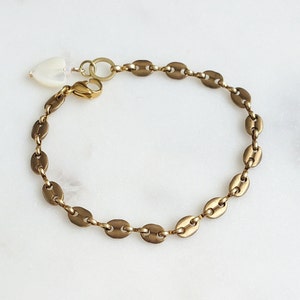 May include: A gold chain bracelet with a small white heart charm. The chain is made of oval links.