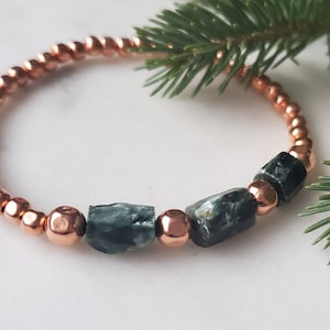 Puede incluir: Un brazalete de cuentas de cobre con tres cuentas de piedras preciosas verdes y negras.