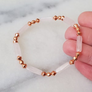 May include: A bracelet made with white rectangular beads and gold-toned spacers. The bracelet is on a hand.