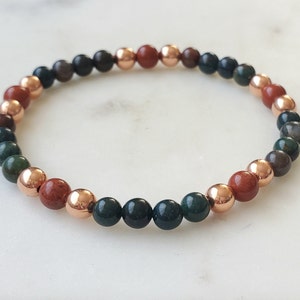 May include: A beaded bracelet with green, brown, and red stones interspersed with copper beads.