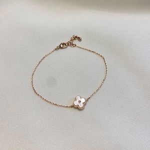 May include: A delicate gold-toned bracelet featuring a four-leaf clover charm with a white mother-of-pearl inlay. The bracelet has a fine chain and an adjustable clasp. The clover charm is centered on the bracelet.