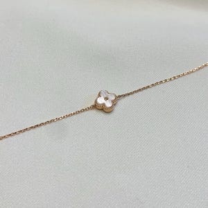 May include: A delicate rose gold bracelet featuring a four-leaf clover charm with a white mother-of-pearl center. The clover is set in a rose gold frame. The bracelet is displayed on a white background.