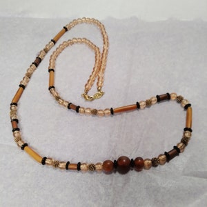 Könnte beinhalten: Eine lange braune und beige Perlenkette mit Holzperlen und goldenen Akzenten. Die Kette hat eine große braune Holzperle in der Mitte.