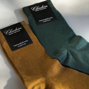 May include: Two pairs of socks, one green and one brown, with black labels that say "Chadrín Italian Cashmere" and "Cashmere & Silk Socks chadrín.me".