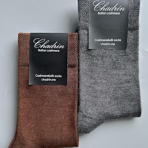以下が含まれることがあります： イタリア製カシミヤソックス2足。濃い茶色とグレー。各ペアには「Chadrin」のブランド名と「Cashmere&silk socks」の文字が入った黒いラベルが付いています。靴下は明るい灰色の表面に表示されています。