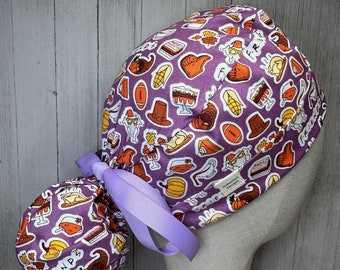 May include: A purple scrub cap featuring a pattern of Thanksgiving-themed illustrations, including turkeys, hats, and desserts. The cap has a light purple ribbon and the word "FRIENDS" printed on the side.