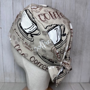 May include: A beige fabric scrub hat with a coffee cup and coffee bean pattern. The hat has a tie at the back. The text "Coffee" is printed on the hat.