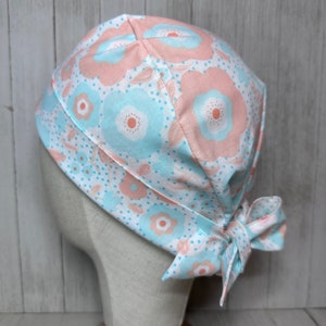 May include: A light blue and pink floral patterned surgical scrub hat with a tie at the back.