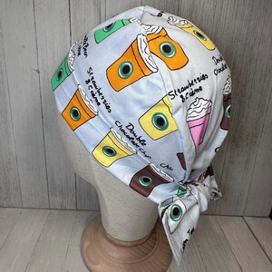 May include: A white surgical scrub hat with a colourful print of coffee cups and the text "Double Chocolate Chip Chai", "Strawberries & Creme", and "Green Tea".