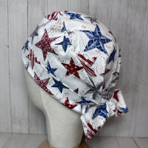 May include: A white scrub hat with a red, white and blue star pattern. The hat has a tie at the back.
