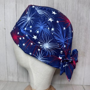 May include: A blue scrub hat with a white and red fireworks pattern. The hat has a tie at the back.